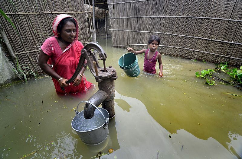 Una mujer y su hija beben agua de un pozo sumergido tras las inundaciones provocadas en la India por subida del nivel de los ríos Rapti, Saryu y Ghaghra