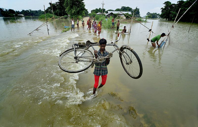 Un ciclista cruza el río a pie con su bicicleta tras las inundaciones provocadas por las intensas lluvias monzónicas en el estado indio de Assam