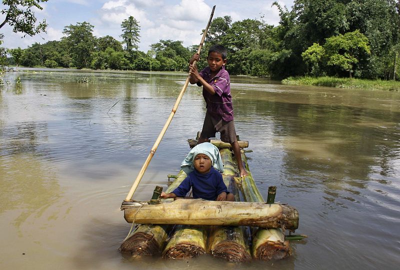 Un niño transporta a un bebé por zonas inundadas en una barca improvisada en el estado de Assam