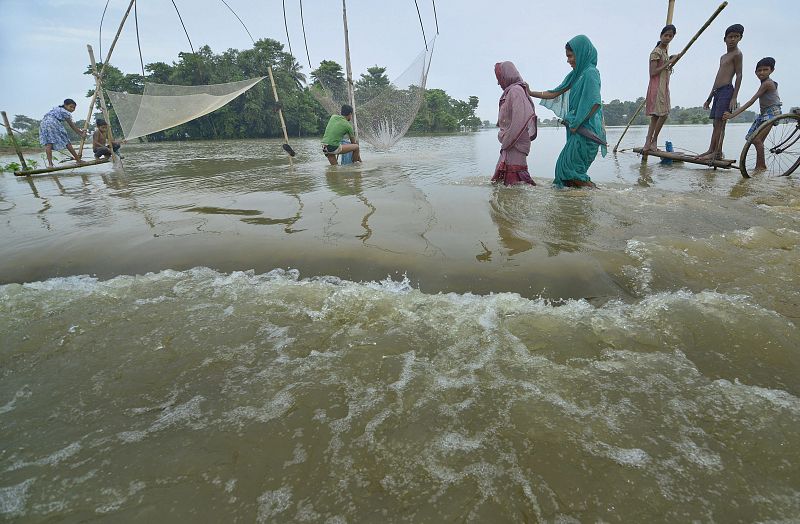 Lugareños cruzan el río tras las inundaciones que han afectado al distrito de Marigaon, en el estado indio de Assam