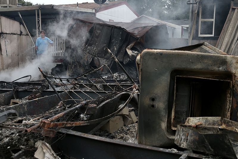Un hombre utiliza una manguera para enfriar los puntos calientes tras un incendio causado por el terremoto.