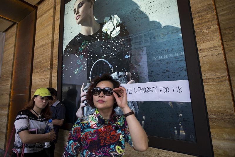 Turistas de la China continental pasan frente a un escaparate con el eslogan "Democracia Real para Hong Kong" en el distrito comercial de Tsim Sha Tsui