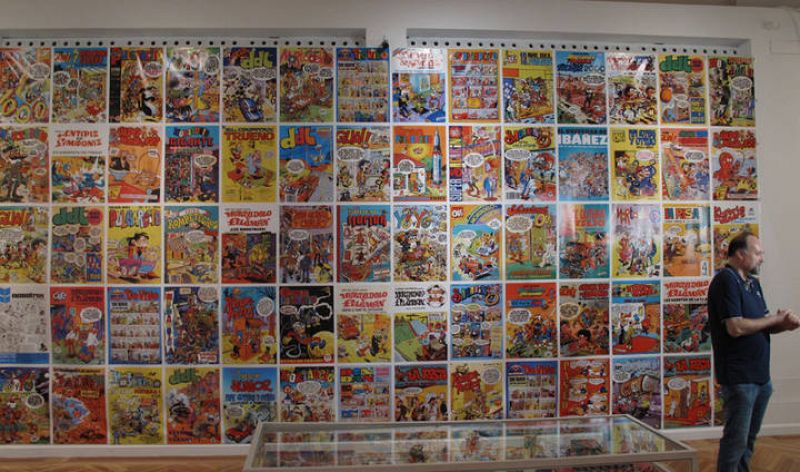 Antoni Guiral delante del mural de portadas de la exposición 'Francisco Ibáñez, el mago del humor' 