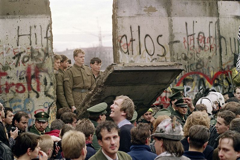 Una fotografía de noviembre de 1989 muestra a una multitud de berlineses occidentales delante del Muro de Berlín, mientras los guardias fronterizos de Alemania Oriental demuelen una sección de la pared.