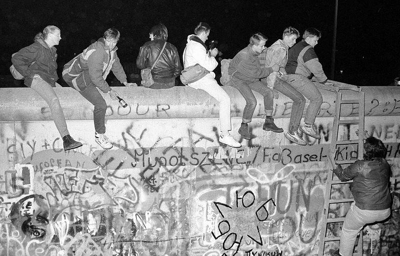 Los ciudadanos de Alemania Occidental se sientan en la parte superior del Muro de Berlín, cerca del ¿Checkpoint Charlie'. 