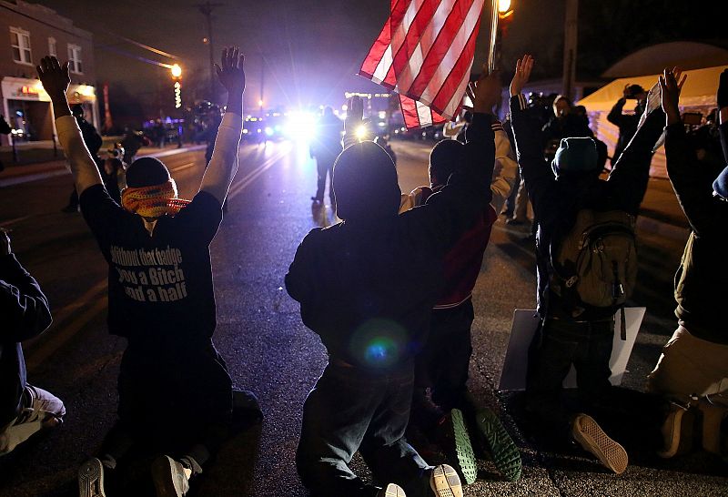 Los manifestantes se arrodillan con las manos en alto frente a vehículos de la policía durante la protesta en Ferguson.
