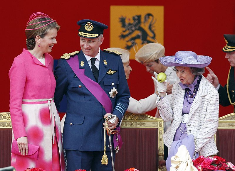 File photo shows Queen Fabiola holding up an apple as Belgium's Crown Prince Philippe and his wife Crown Princess Mathilde (L) talk after the traditional military parade on National Day in front of the Royal Palace in Brussels