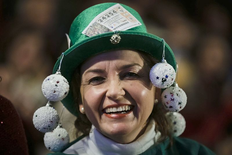 Una mujer ataviada con un sombrero de disfraces, en el Teatro Real, lleva adosado uno de los números que juega en el sorteo extraordinario de la lotería de Navidad 2014.