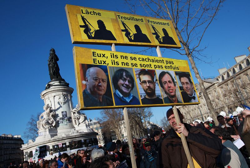 Un hombre sostiene un cartel con varios retratos de las víctimas mortales en la revista de 'Charlie Ebdo' en París.