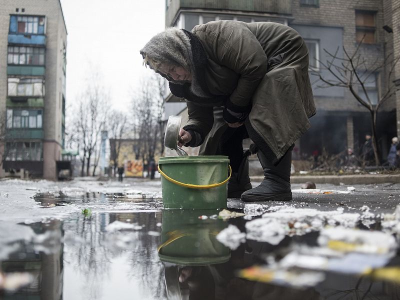 Una anciana recoge agua de un charco en la calle en Donetsk porque los combates han cortado el suministro.