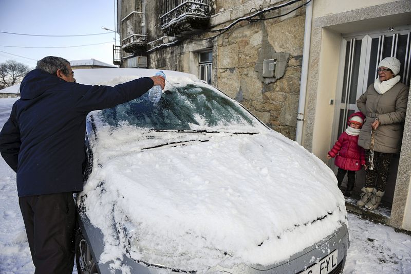 Un hombre echa agua para descongelar el parabrisas de su coche en Vilavella (Galicia).