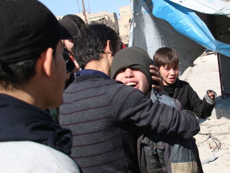 Varios niños se consuelan, asustados aún, tras el impacto de un barril bomba en un barrio de Alepo. 