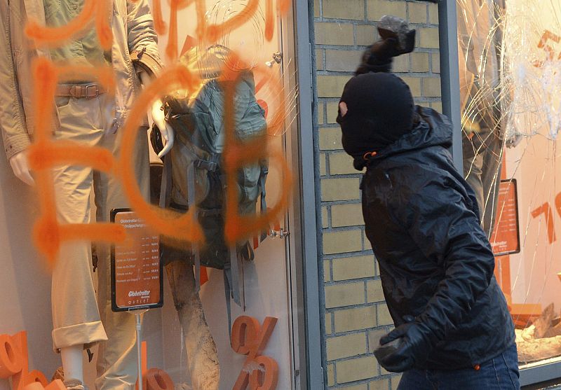 Un manifestante se prepara para lanzar una piedra contra un escaparate