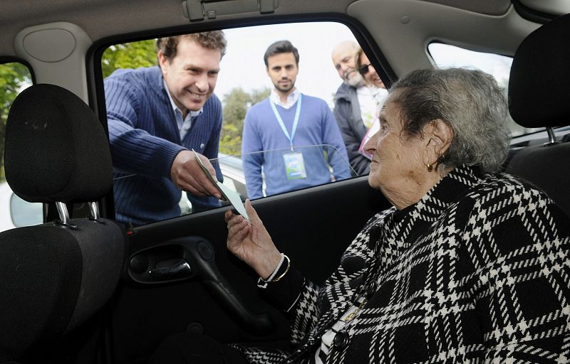 Una anciana de 98 años ejerce su derecho al voto entregando su papeleta al presidente de la mesa, en el municipio sevillano de Tomares.