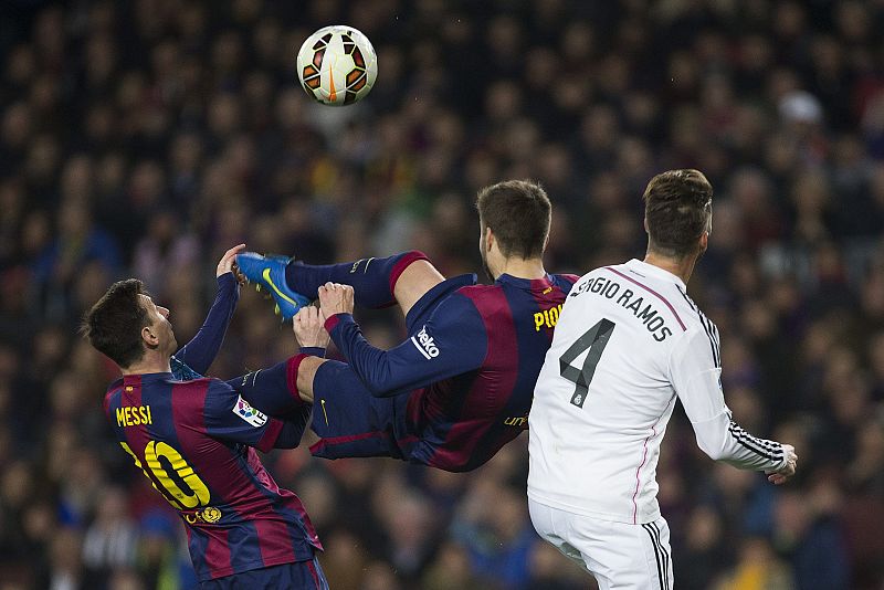 Gerard Piqué (c) intenta rematar de chilena ante su compañero, el argentino Leo Messi (i) y el defensa del Real Madrid, Sergio Ramos.