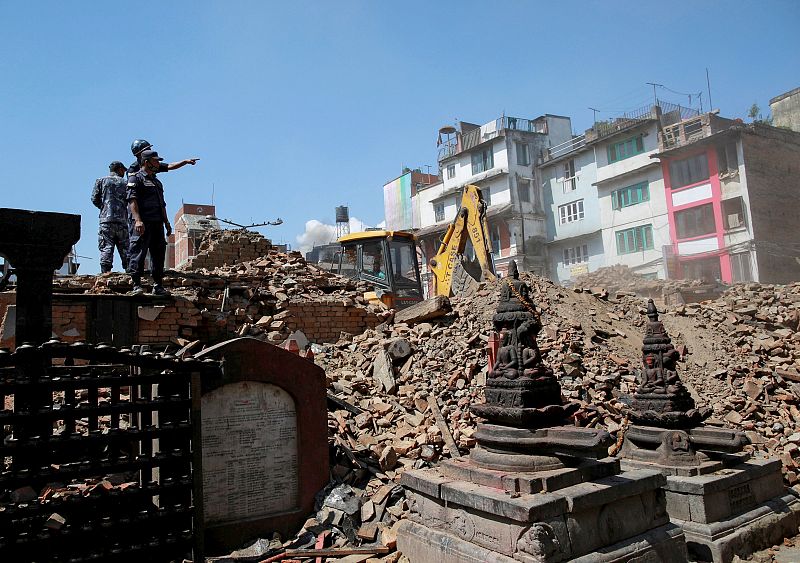 Nepalese police personnel look on as an excavator is used to dig through rubble to search for bodies following Saturday's earthquake in Kathmandu, Nepal