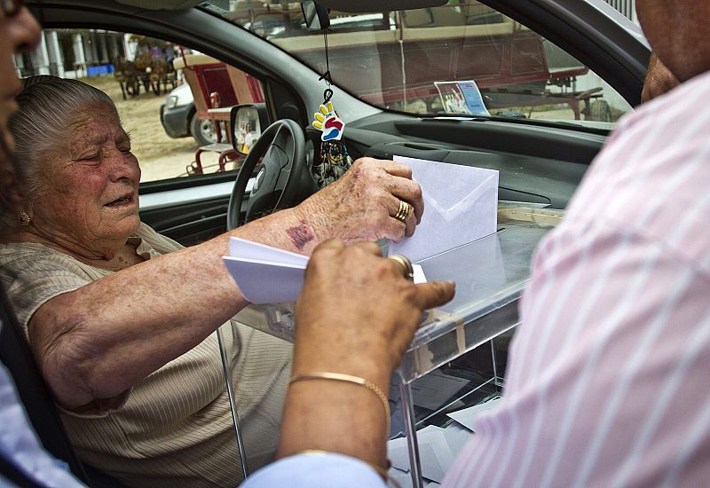 Una mujer con problemas de movilidad ejerce su derecho al voto en la puerta del colegio electoral de la aldea almonteña de El Rocío (Huelva).