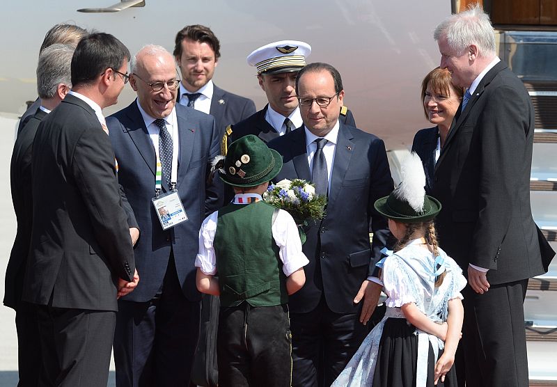 El presidente francés, François Hollande, es recibido por dos chicos vestidos con trajes regionales a su llegada al aeropuerto de Múnicn, antes de asistir a la cumbre del G7.