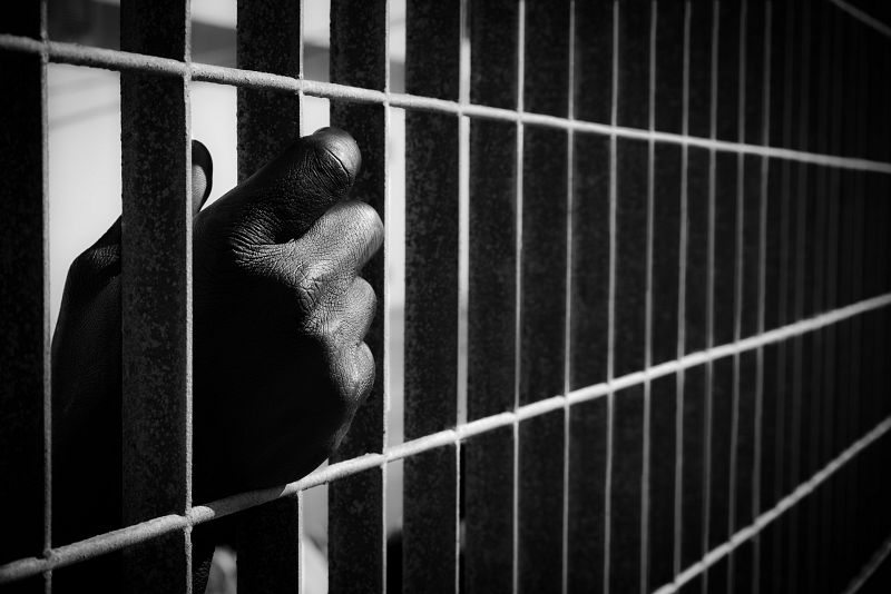 Inmigrante espera la salida del Ferry hacia Sicilia, aferrándose a la valla del puerto de Lampedusa.