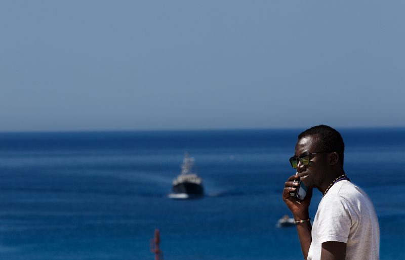 Joven africano hablando por teléfono con las aguas de Lampedusa como telón de fondo.