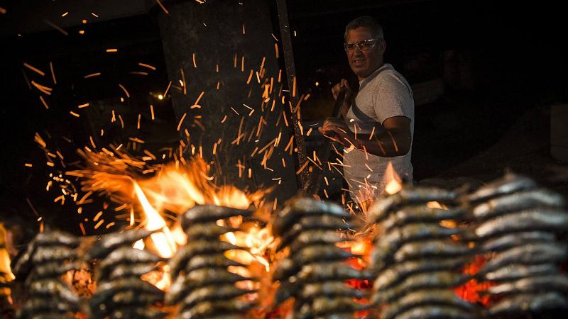 Un hombre prepara unos espetos junto a una hoguera durante las celebraciones de la noche de San Juan.