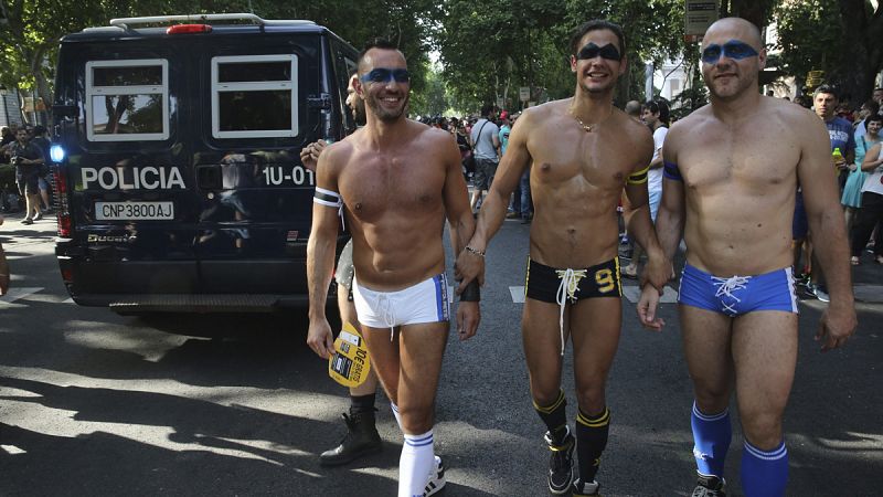 Tres participantes caminan en la manifestación del Orgullo Gay en Madrid delante de un furgón policial