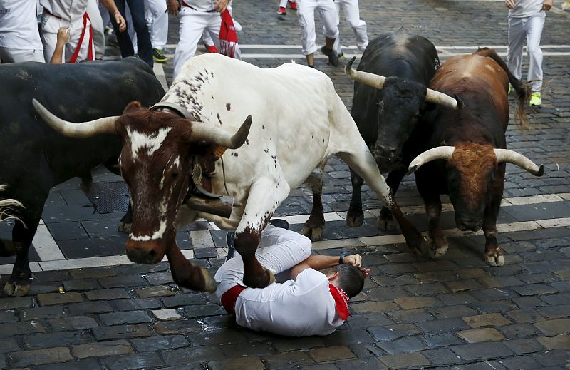 A steer jumps over a fallen runner as two Jandilla fighting bulls follow behind at the Mercaderes curve during the first running of the bulls of the San Fermin festival in Pamplona