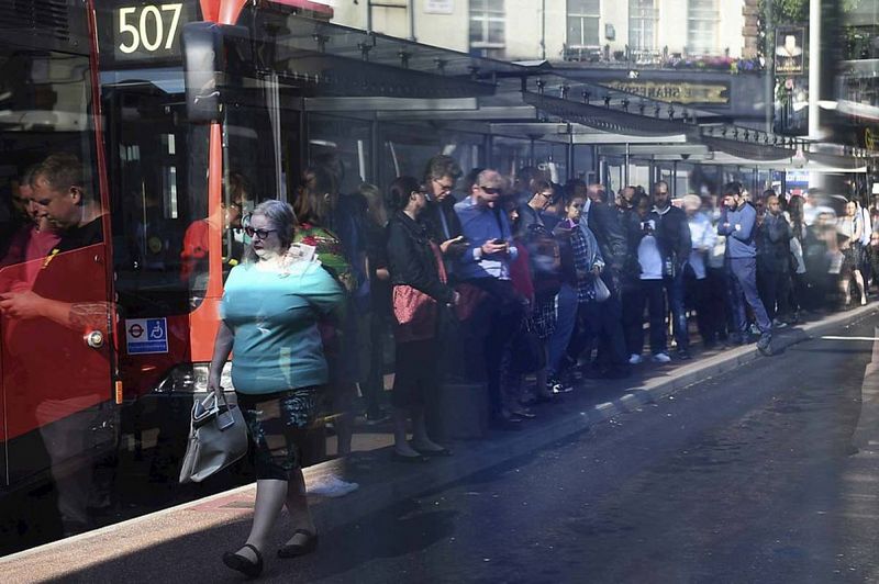 Reflejo, en una marquesina de una parada de un autobús, de los usuarios del transporte público que guardan largas colas para tomar un autobús