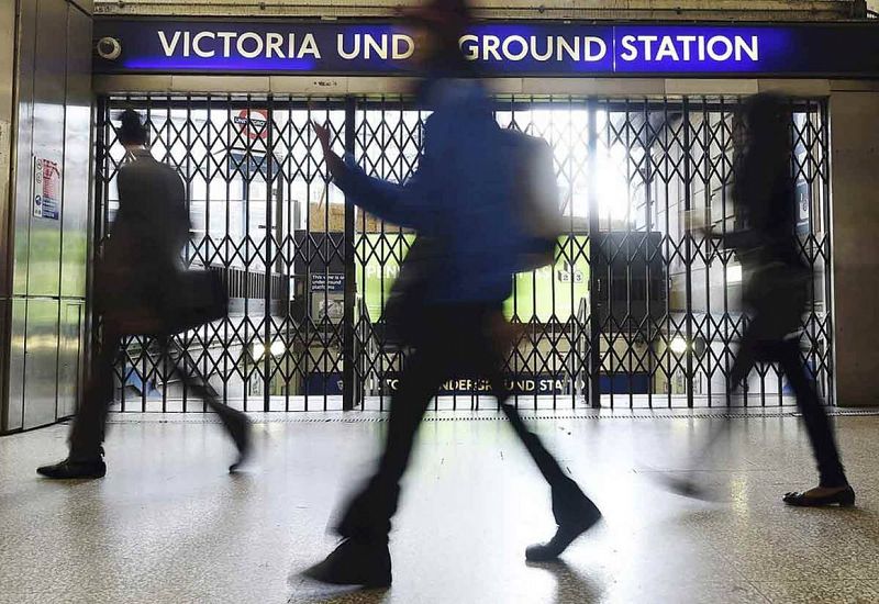 Usuarios del transporte público pasan por delante de las puertas cerradas de la estación de metro de Victoria de Londres