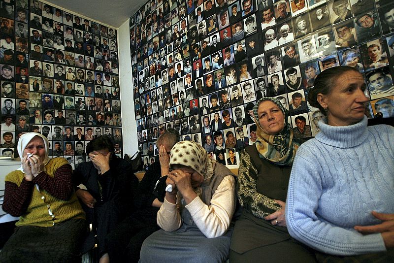 Mujeres enfrente de la televisión contemplan la decisión de la Corte Internacional de Justicia que reconocía la masacre como genocidio en 2007. Detrás, cientos de fotos de los desaparecidos cubren la pared de la habitación.