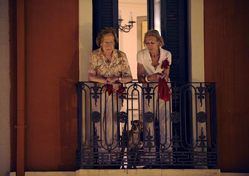 Dos mujeres contemplan a la multitud que canta el "Pobre de mí" desde un balcón.
