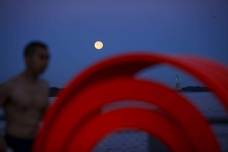 The effect known as Blue Moon is seen next to the Statue of Liberty while a man jogs in New York