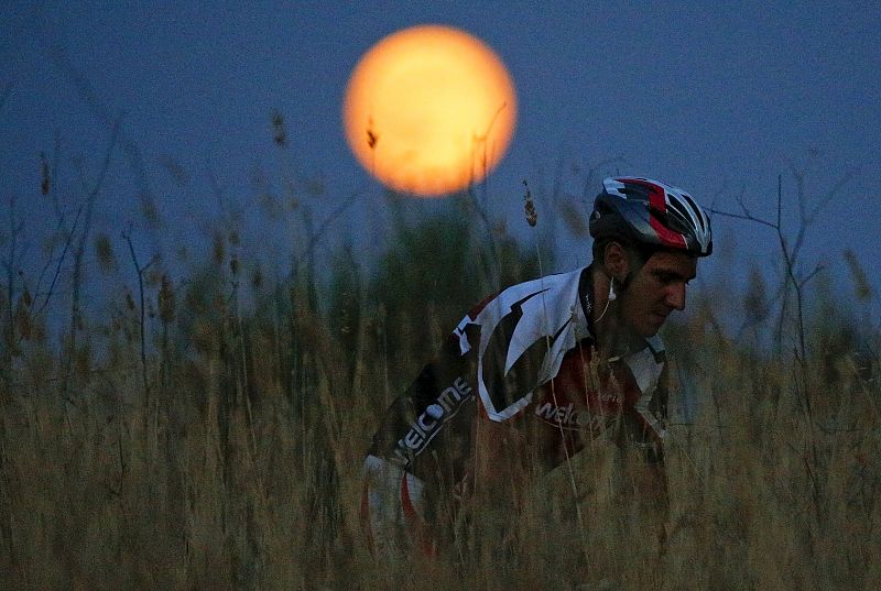 Un ciclista circula con la luna llena de fondo en un parque en Roma