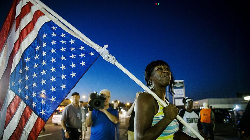 Una mujer porta una bandera estadounidense desplegada al revés, un símbolo de emergencia nacional