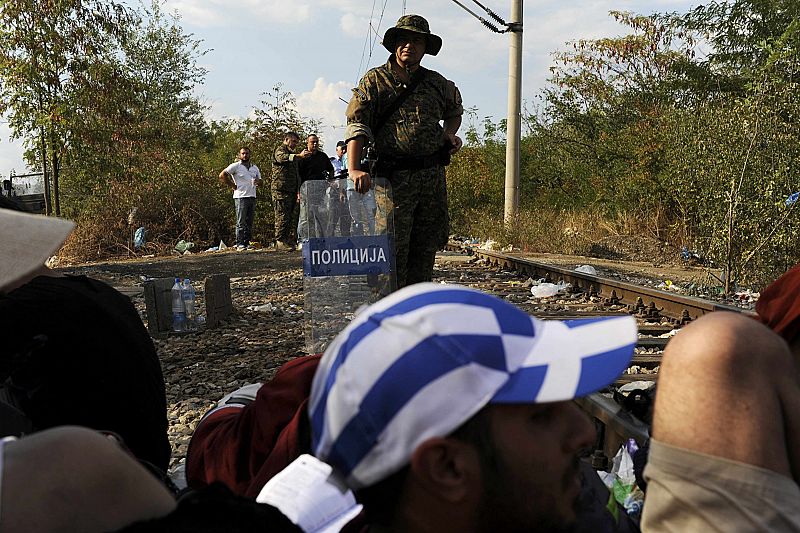 Macedonian police officer stands guard on the borderline with Greece as migrants rest on the Greek side of the borders