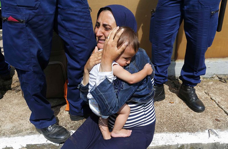 Hungarian policemen stand by a migrant holding a baby at the railway station in the town of Bicske