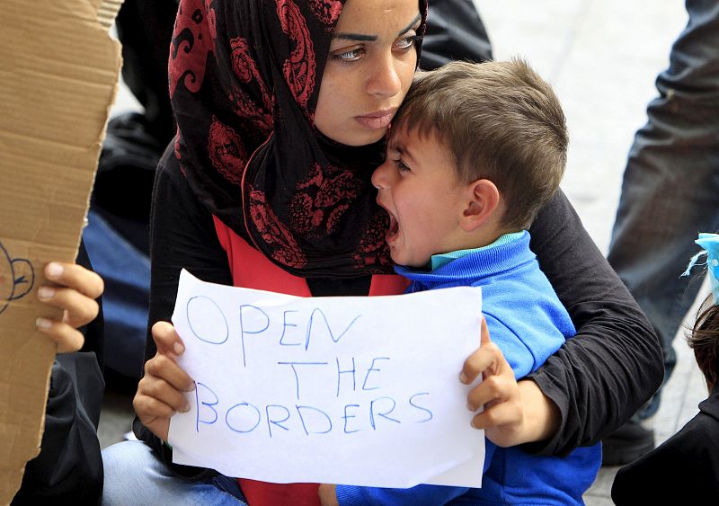 Una mujer, con su hijo, porta un papel en el que pide que se abran las fronteras.