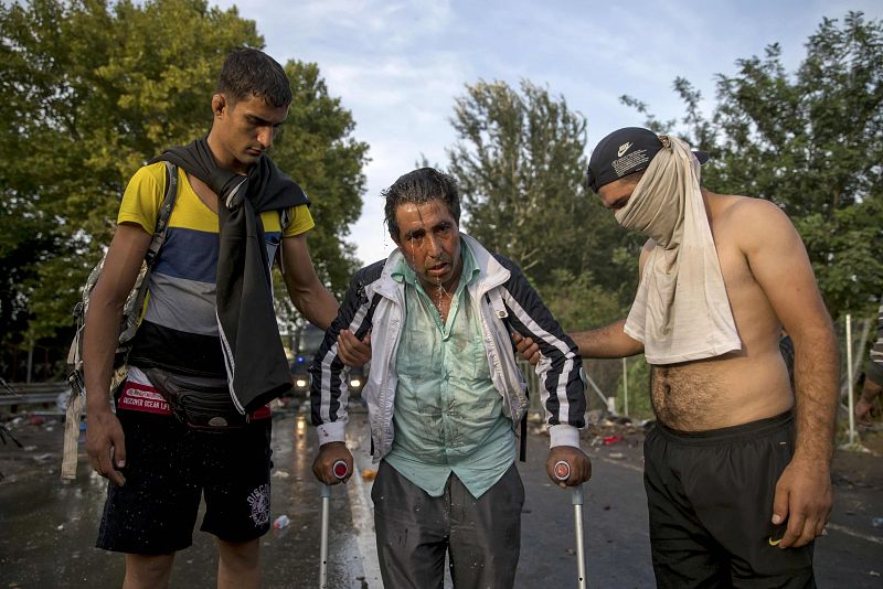 Dos refugiados ayudan a otro después del enfrentamiento con la policía húngara