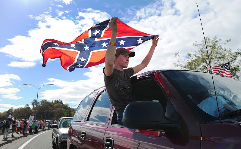 Un hombre porta una bandera confederada como señal de protesta ante la visita de Obama.