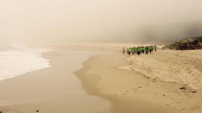 Un grupo de "trasnos" avanza por una playa envuelta en bruma en una de las etapas de O Camiño dos Faro