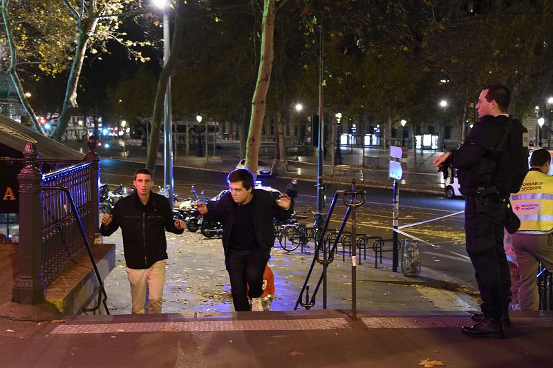 Dos hombres son evacuados de la Plaza de la República de París bajo la vigilancia de un agente de policía tras producirse varios tiroteos.