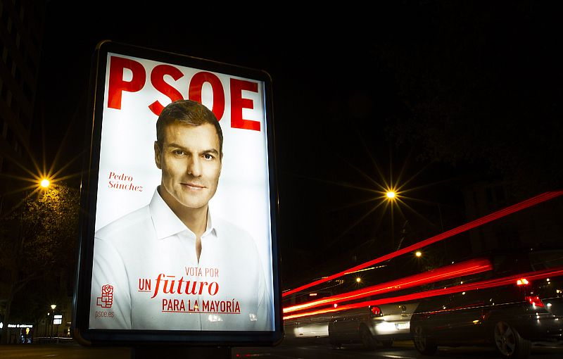 Los coches circulan en Palma de Mallorca ante un póster electoral del candidato del PSOE, Pedro Sánchez.