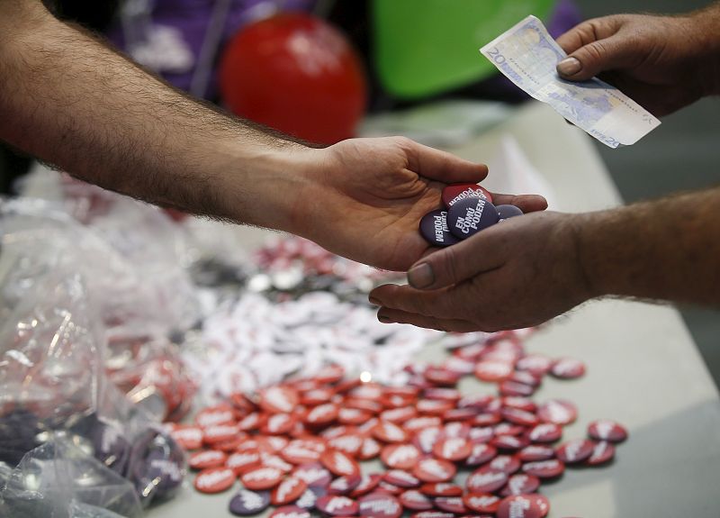 Un simpatizante de Podemos compra chapas en un mitin de la formación en Barcelona.