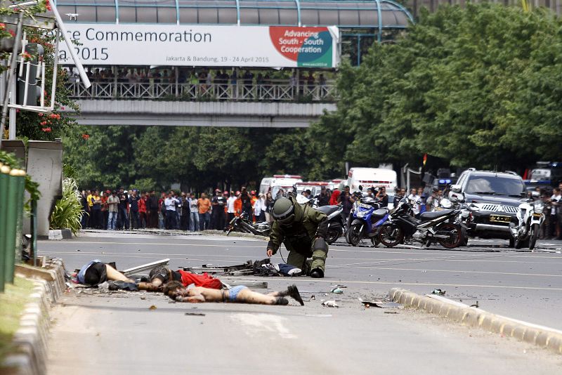 Un artificiero de la policía inspecciona uno de los cadáveres que permanecen en el suelo en el lugar donde se ha producido una explosión en la capital de Indonesia.