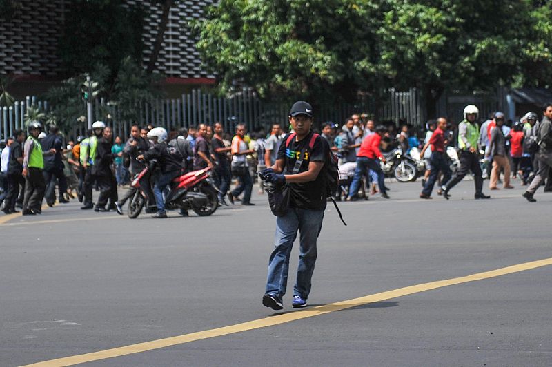Un hombre, identificado posteriormente por la prensa local como uno de los asaltantes de Yakarta, empuña una pistola mientras la gente huye a su espalda