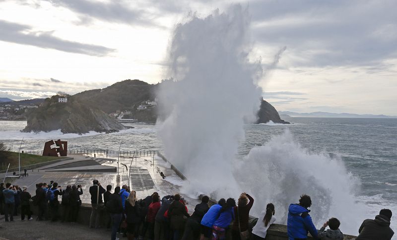 Varias personas observan como una gran ola rompe contra el Paseo Nuevo de San Sebastián.