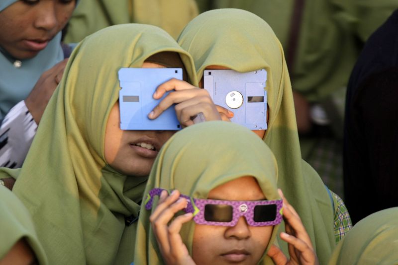 Niños utilizan discos magnéticos para observar el eclipse parcial de sol desde Banda Aceh (Indonesia).