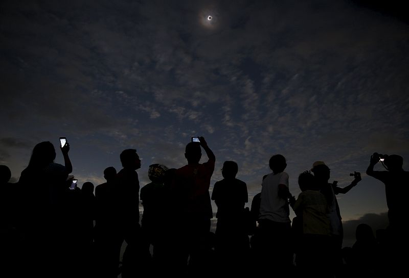 Un grupo de gente toma fotografías y observa el eclipse desde una playa de Ternate, en Indonesia.