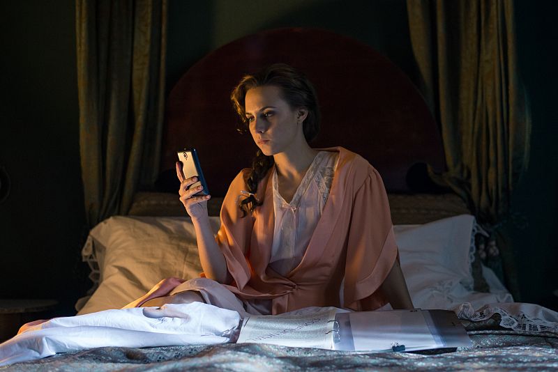 Amelia en la cama revisa unos informes pero está a punto de llamar a una persona