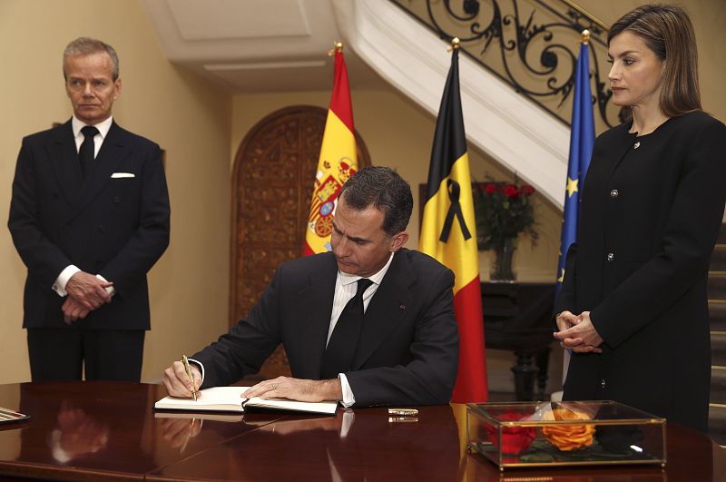 El rey Felipe, en presencia de la reina Letizia y del embajador de Bélgica en España, Pierre Labouverie (i), firma en el libro de condolencias en la residencia del embajador, en Madrid.